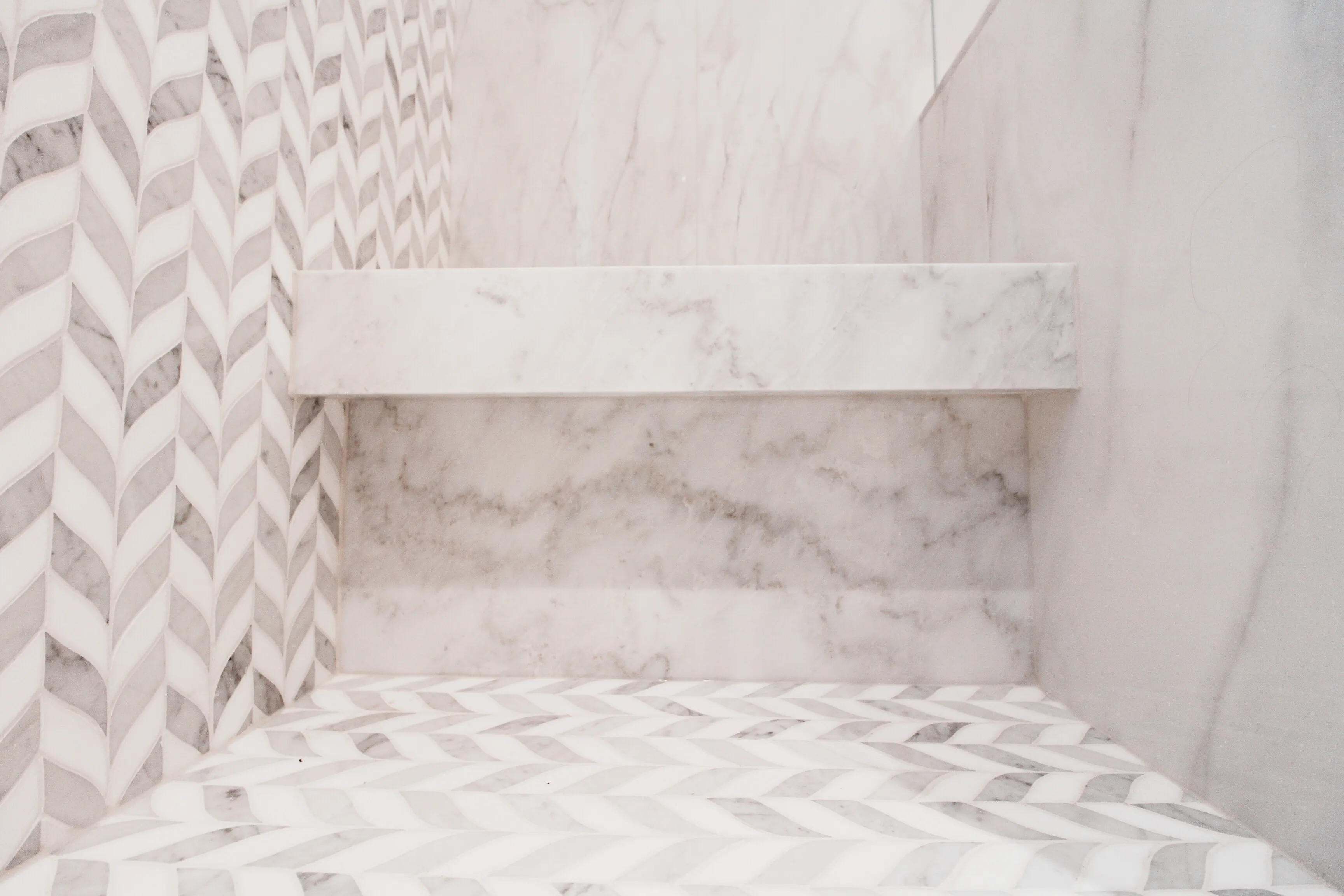 A luxurious white marble bathroom featuring an elegant chevron pattern on the floor.
